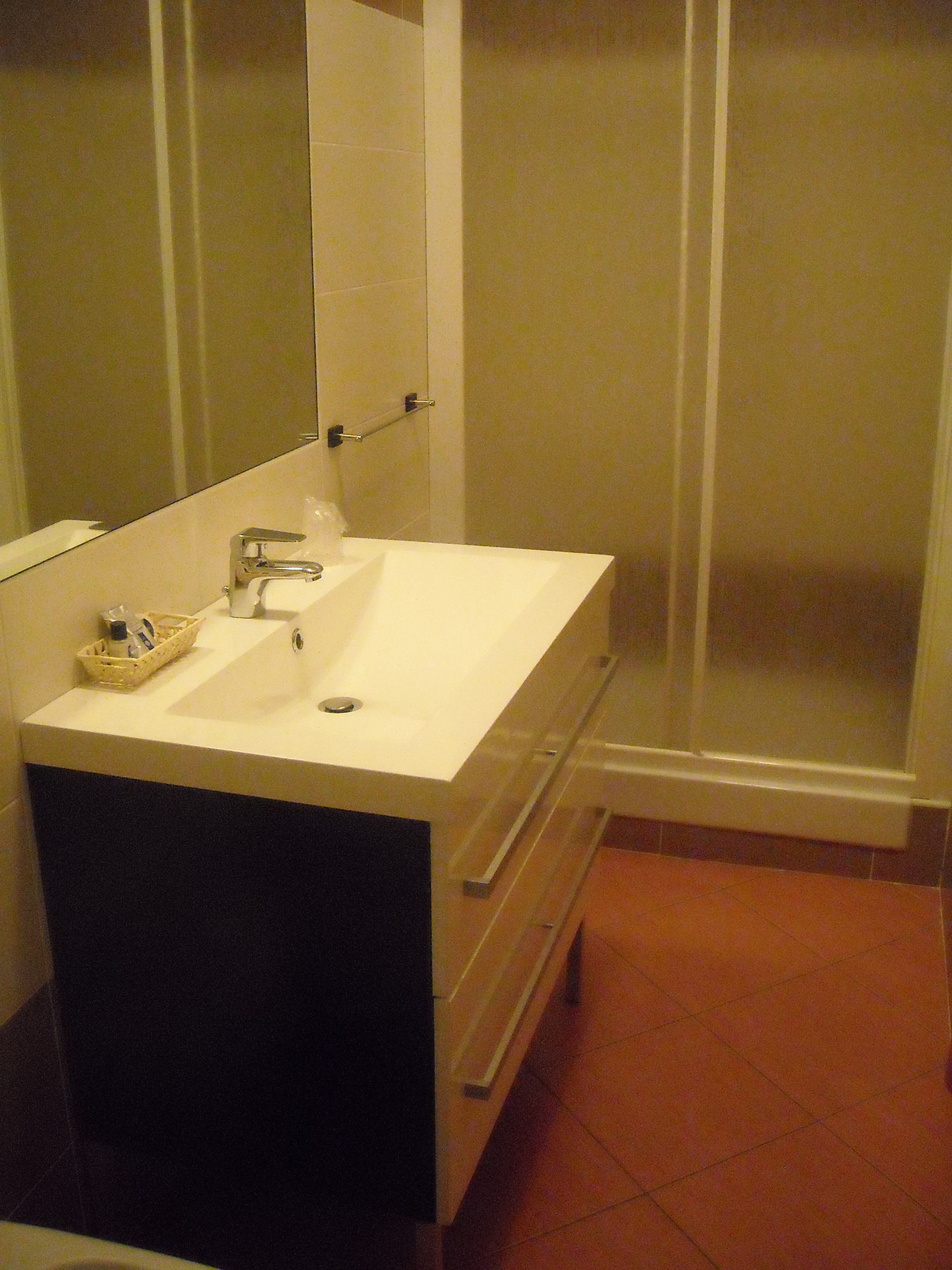 A bathroom with a white sink, a mirror, a towel rack, and a shower enclosure.