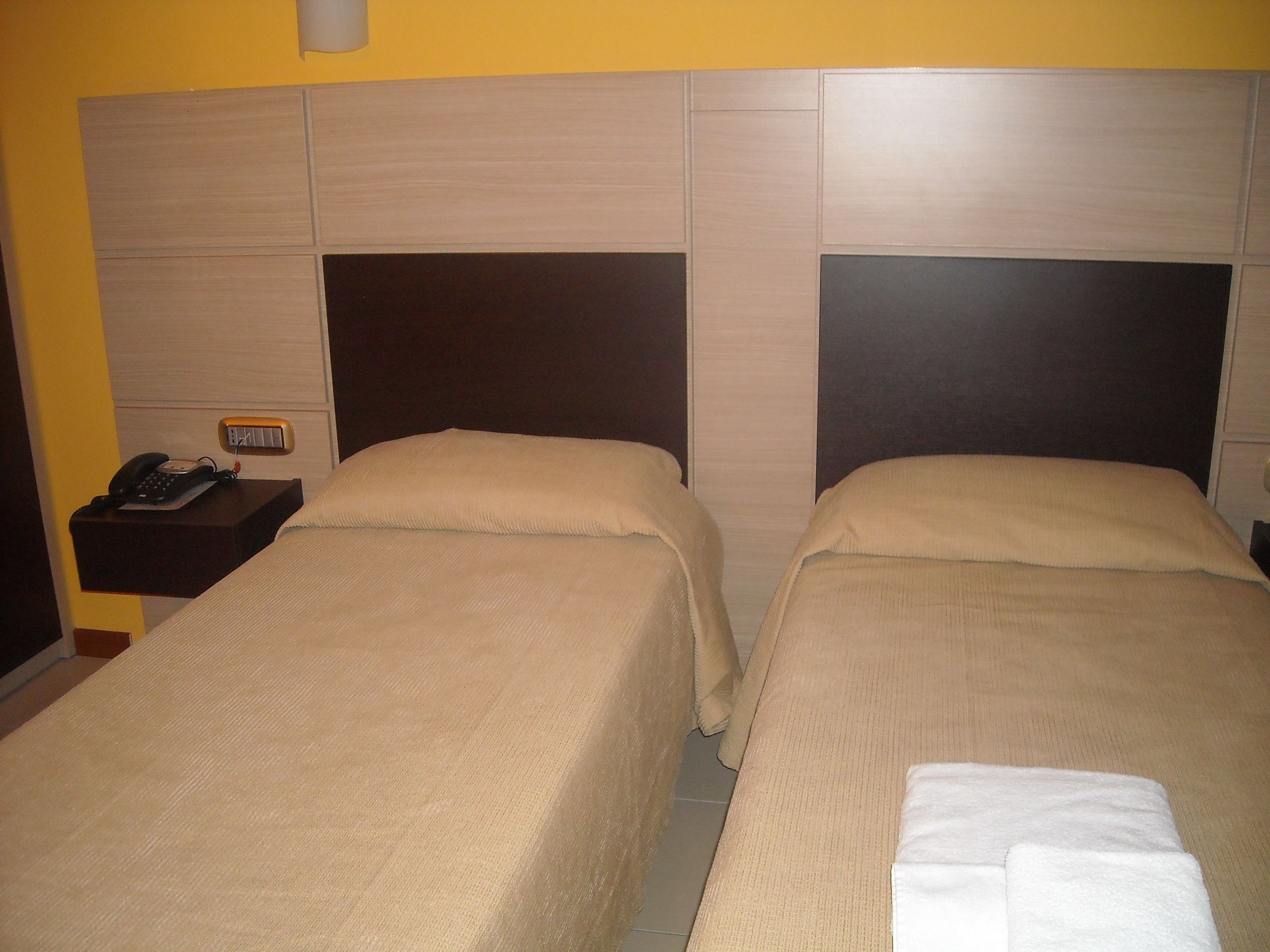 A hotel room with two beds, each with a headboard and a bedside table with a phone.