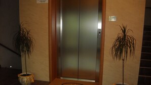An elevator with a sign above it that reads "Use the lift, use the stairs." There is a doormat with "Lapiana Hotel" written on it, and two potted plants on either side of the elevator. - Hotel La Piana (Tito)
