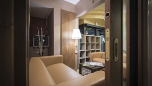A modern hotel room with a sofa, a small table with magazines, a lamp, and a bookshelf. - Hotel La Piana (Tito)