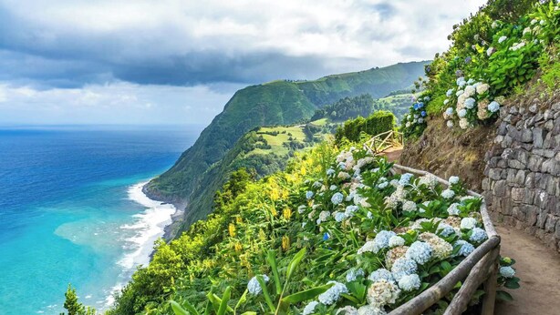 A coastal landscape with a stone pathway, lush greenery, and a view of the ocean. - Hotel Vale Verde (Povoacao)