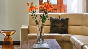 A living room with a beige sofa, a coffee table with a book, and a vase with orange flowers. - Hotel Vale Verde (Povoacao)