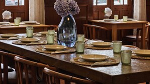 A dining area with wooden tables and chairs, a vase with flowers, and a painting on the wall. - Hotel Vale Verde (Povoacao)