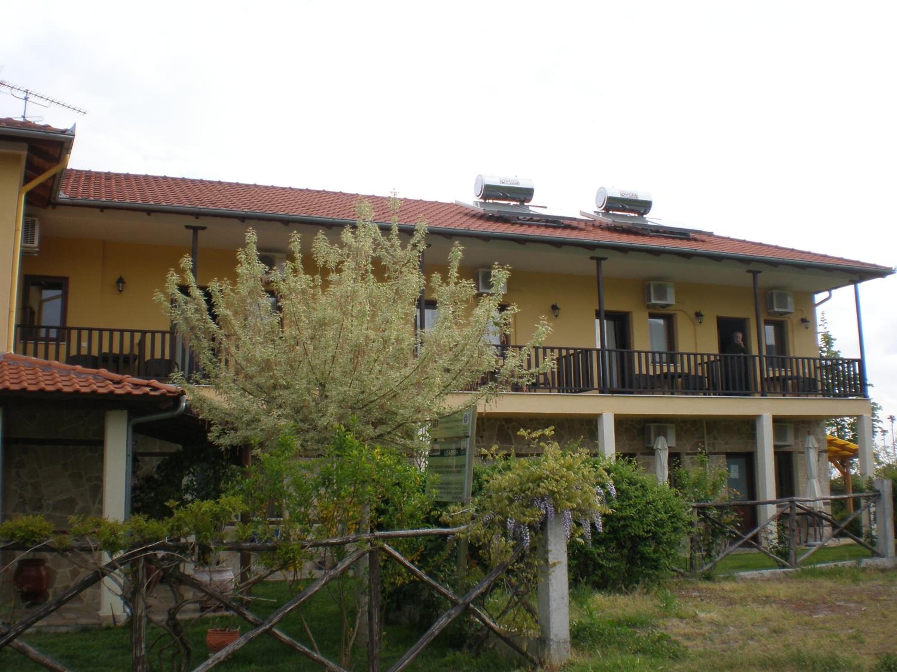 A two-story building with a yellow facade, balconies, and a garden area.
