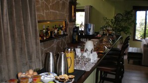 Una barra de desayuno con fruta, café y té. Se ven sillas y un sofá al fondo.