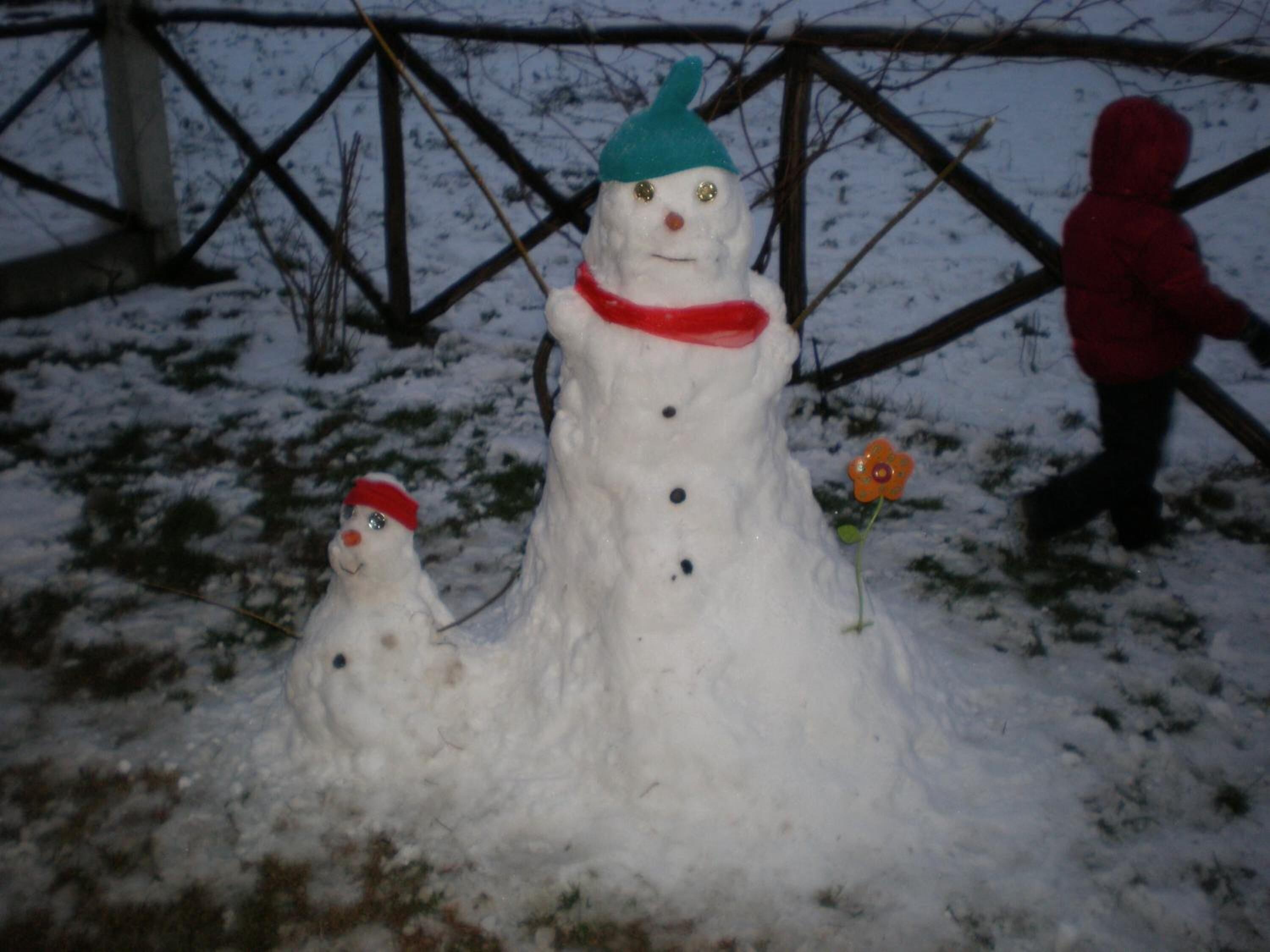 A snowman with a red scarf and a blue hat, and a smaller snowman with a red hat.