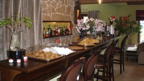 Zona de bar con pared de piedra, barra con diferentes botellas, una bandeja de comida y un arreglo floral.