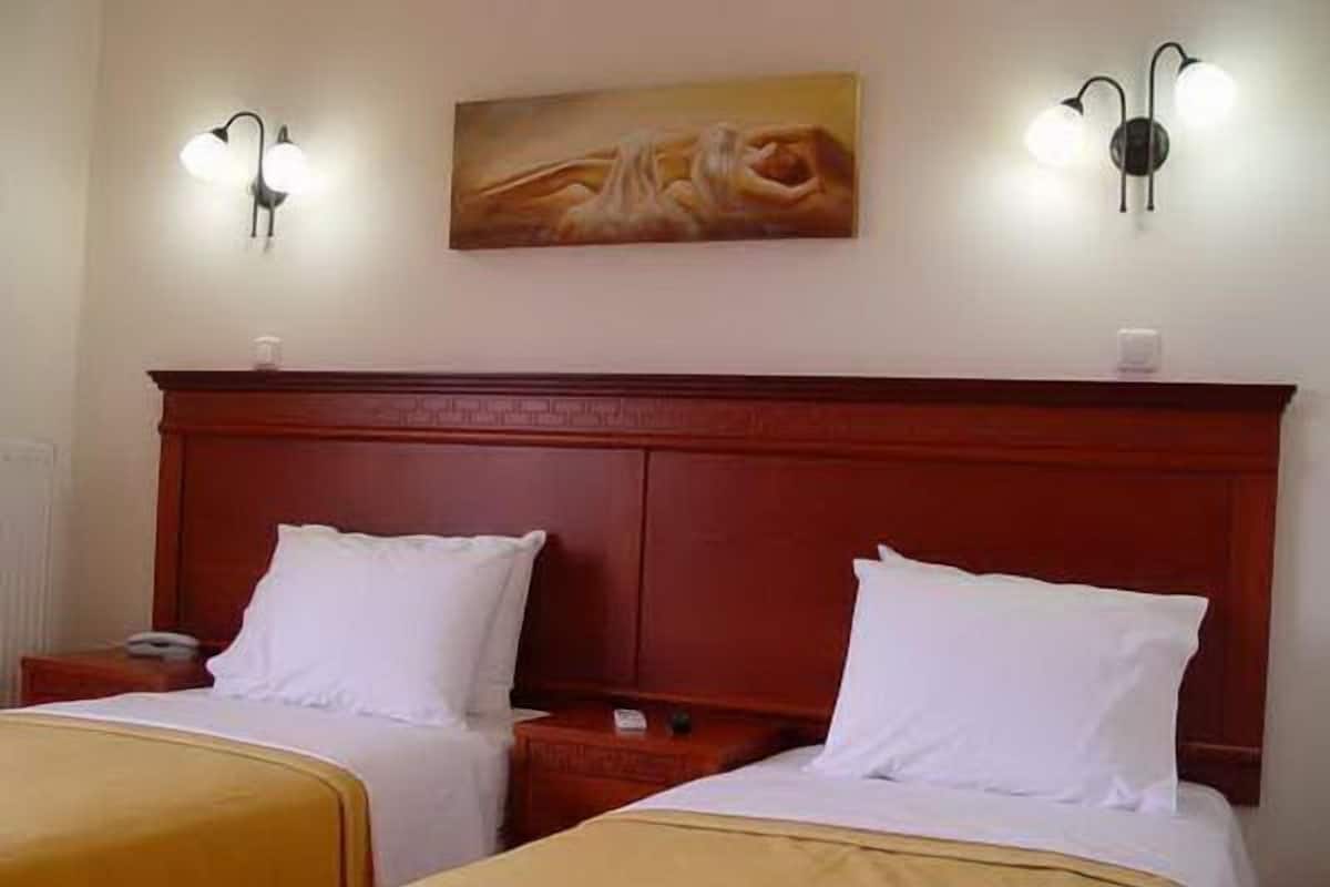 Ein Hotelzimmer mit zwei Betten, einem Holz-Kopfteil, zwei Wandleuchten und einem Gemälde an der Wand.
