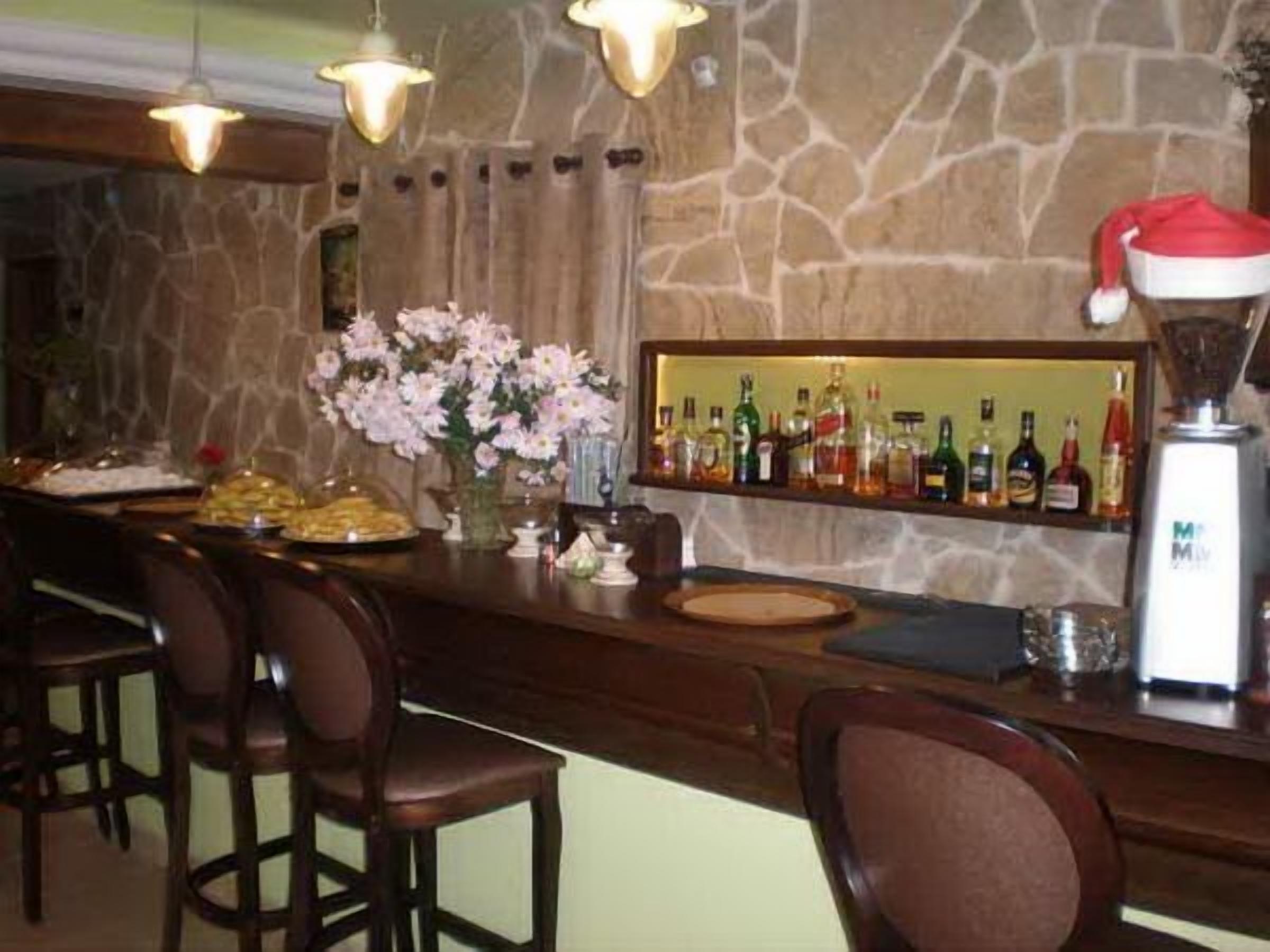 A bar area with a stone wall, multiple hanging light fixtures, a variety of liquor bottles, and a Santa hat on a blender.