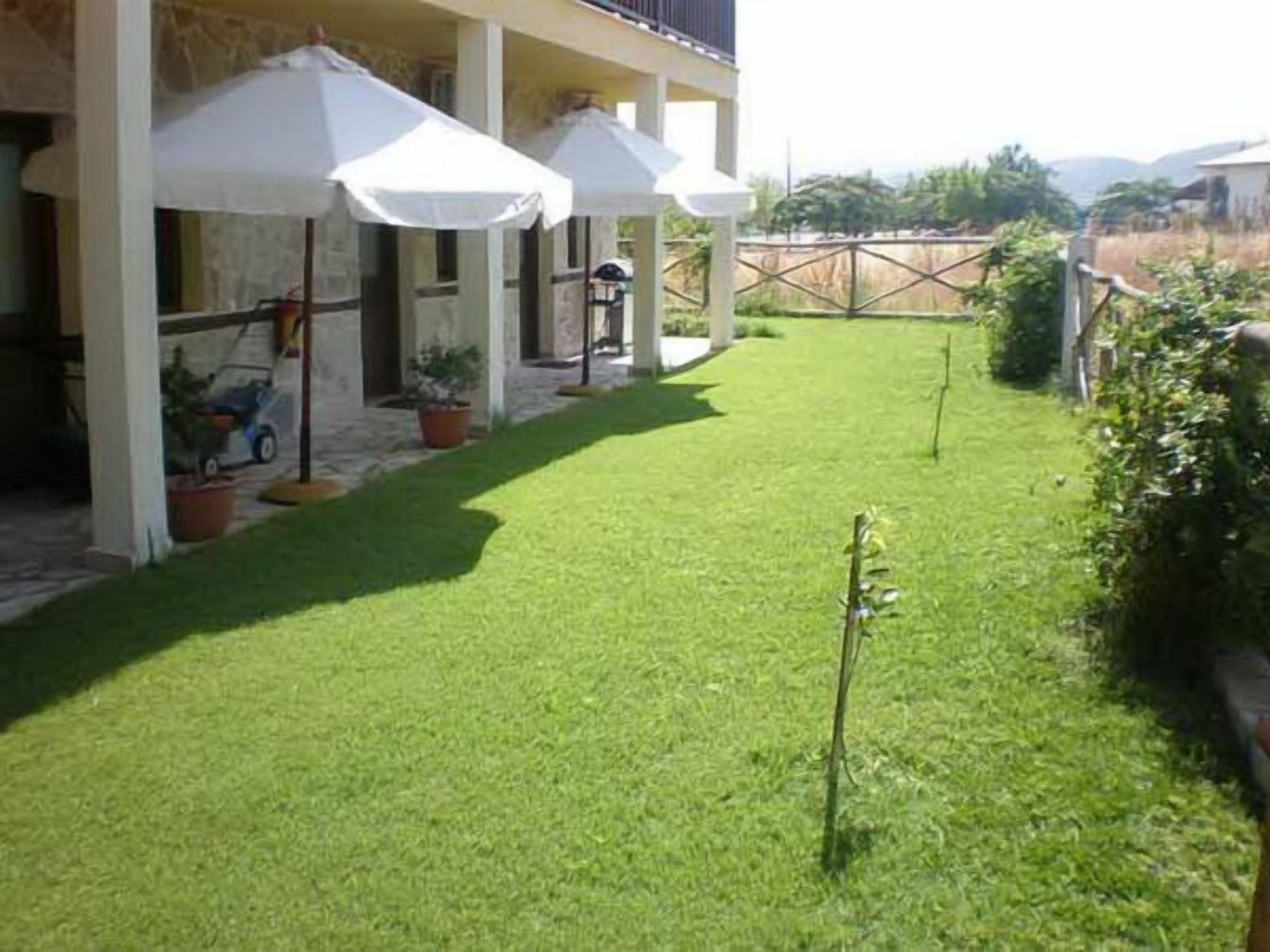 Ein gepflegter Patio-Bereich mit Rasenfläche, Gartenmöbeln und Sonnenschirmen, die Schatten spenden.