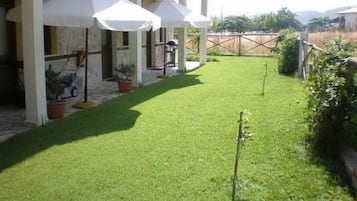 Ein gepflegter Patio-Bereich mit Rasenfläche, Gartenmöbeln und Sonnenschirmen, die Schatten spenden.