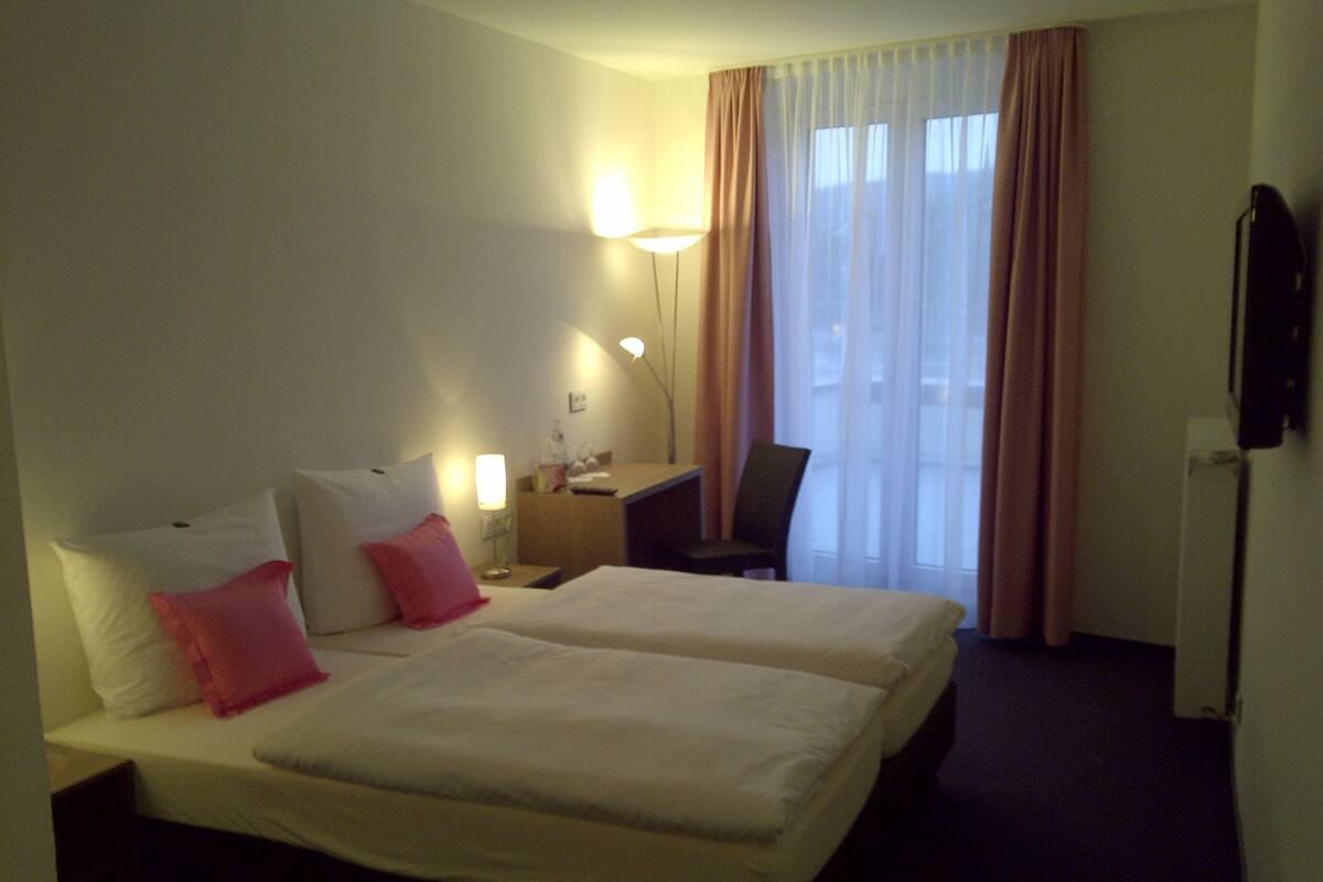 A hotel room with two beds, a desk, a chair, a lamp, and a television.