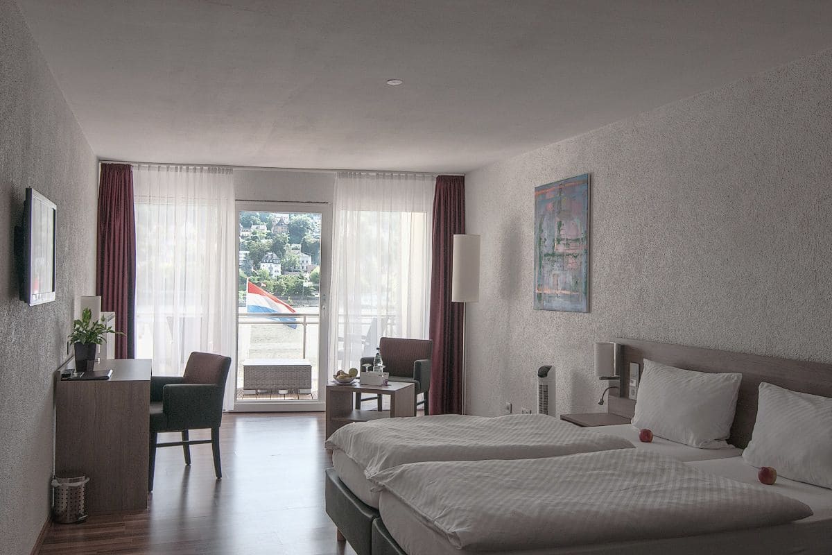 A hotel room with a bed, a desk, a chair, a lamp, and a painting on the wall.