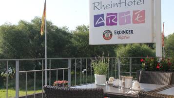Mesa de RheinHotel al aire libre con sillas de mimbre, una planta en maceta y un cartel.