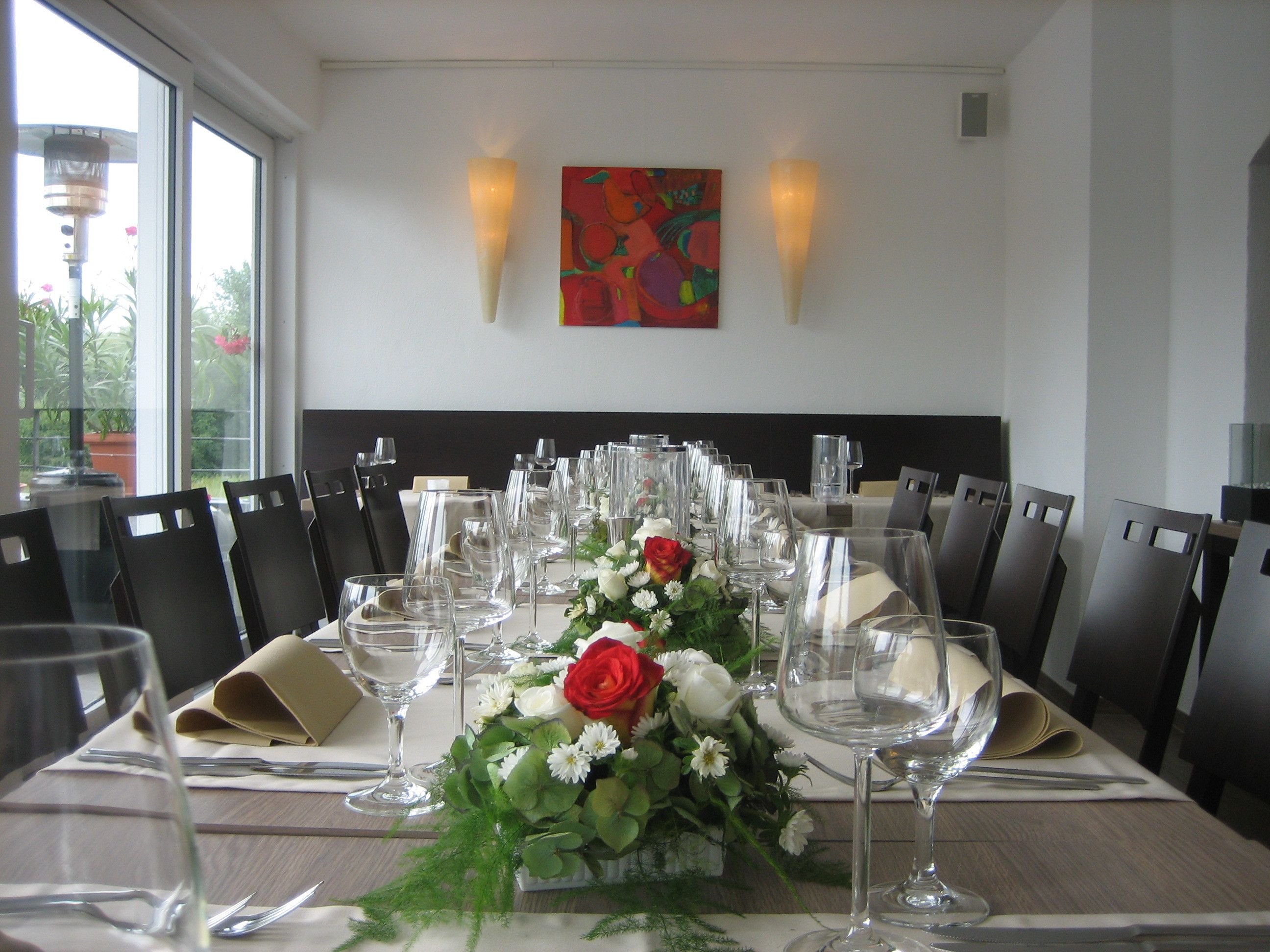 A dining table set with multiple chairs, a centerpiece of flowers, and a painting on the wall.