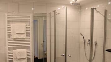 Een moderne badkamer met een douchecabine van glas, een witte handdoekhouder en een toilet in de achtergrond.