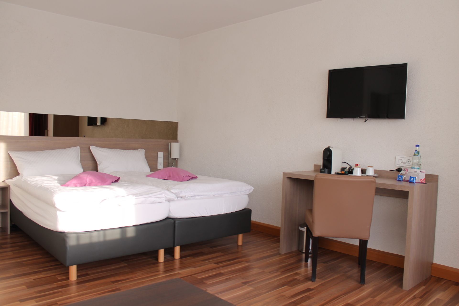 A hotel room with a bed, a desk, a chair, a TV, and a small kitchenette area.