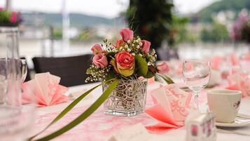 A table set with a glass vase of flowers, a glass of water, and a white cup.
