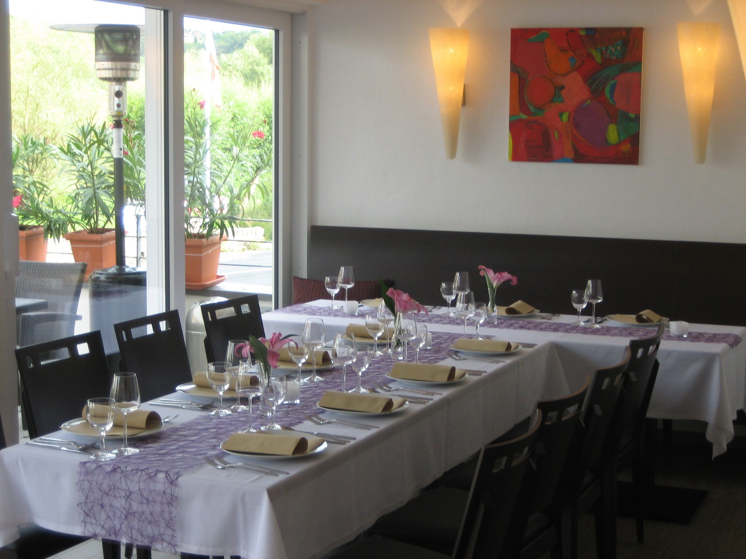 A restaurant with tables set for dining, featuring a view of greenery through the windows.