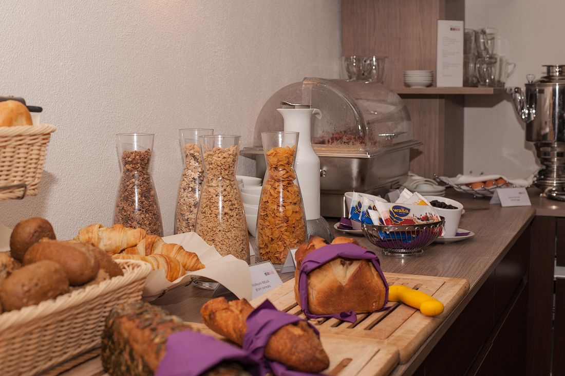A breakfast buffet with various breads, pastries, and cereal options.