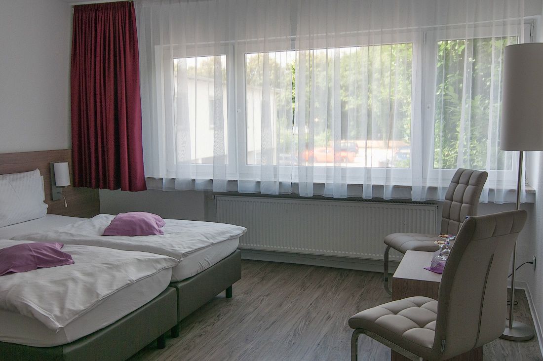 A hotel room with two beds, a chair, a table, and a window with curtains.