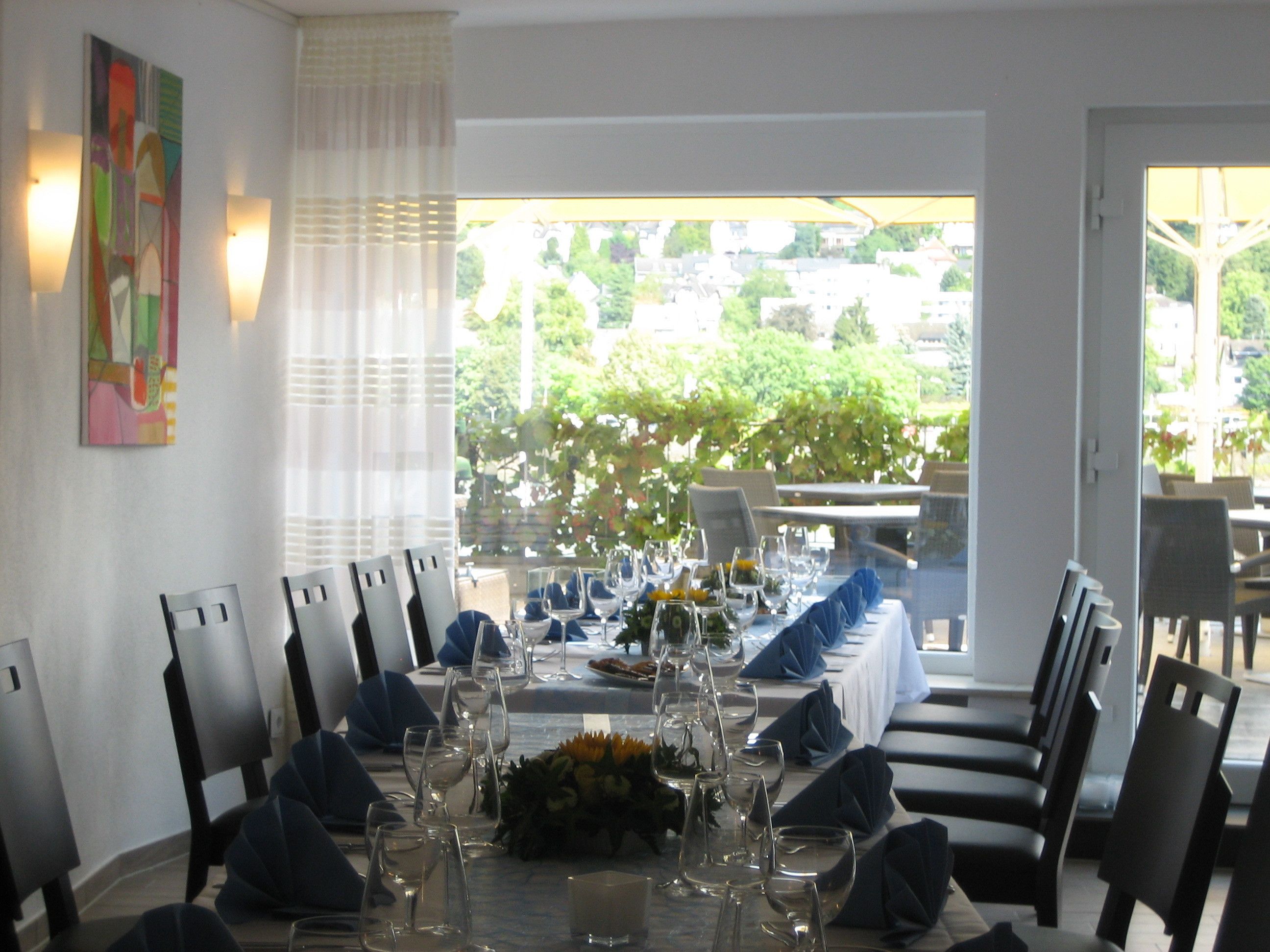 Comedor con una larga mesa preparada para una comida, sillas y vistas al exterior con vegetación.