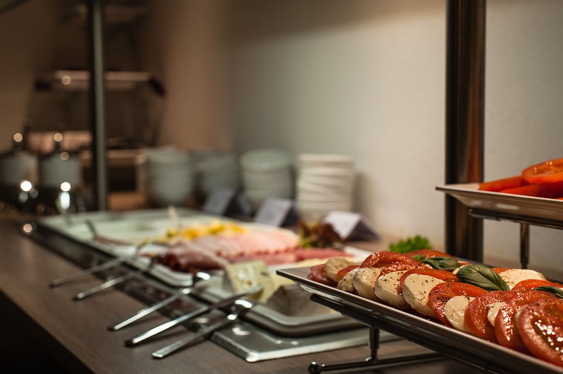 A buffet with various food options, including sliced tomatoes and mozzarella, arranged on metal serving boards.