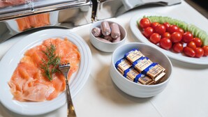 A buffet with plates of salmon, sausages, cherry tomatoes, and packaged food items.