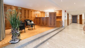 A hotel lobby with wooden paneling, a reception desk, a seating area with a chair and table, and a potted plant.