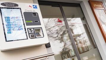 Een incheckautomaat met een digitaal scherm, een bord met een hotelnaam en een bord voor een restaurant.