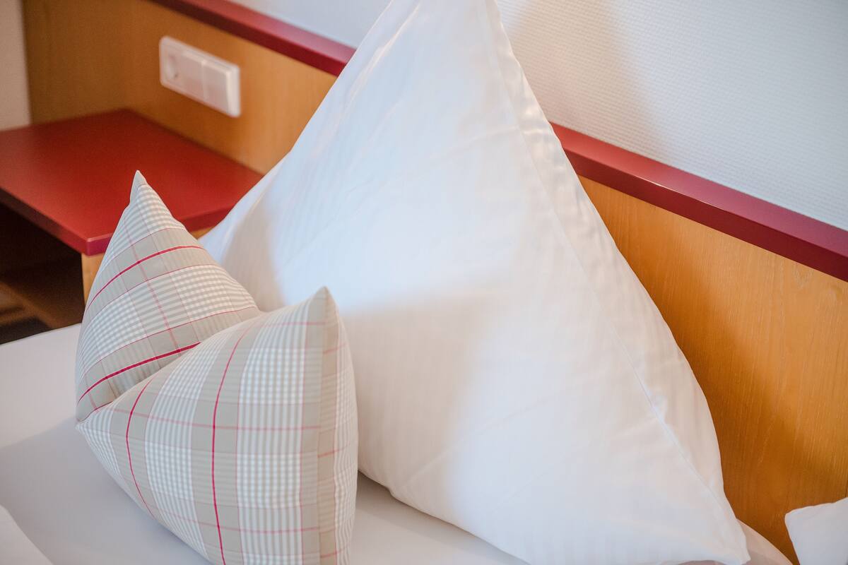 A bed with two pillows, one with a checkered pattern and one plain white.