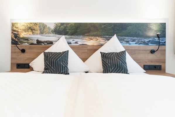 A bed with a view of a river and forest, two pillows, a lamp, and a wall-mounted control panel.