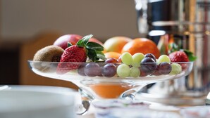 A fruit platter on a clear glass stand with various fruits including strawberries, grapes, and apples.