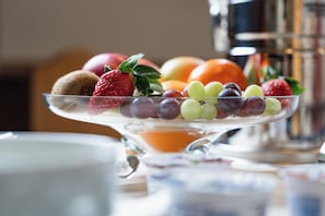 A fruit platter on a clear glass stand with various fruits including strawberries, grapes, and apples.