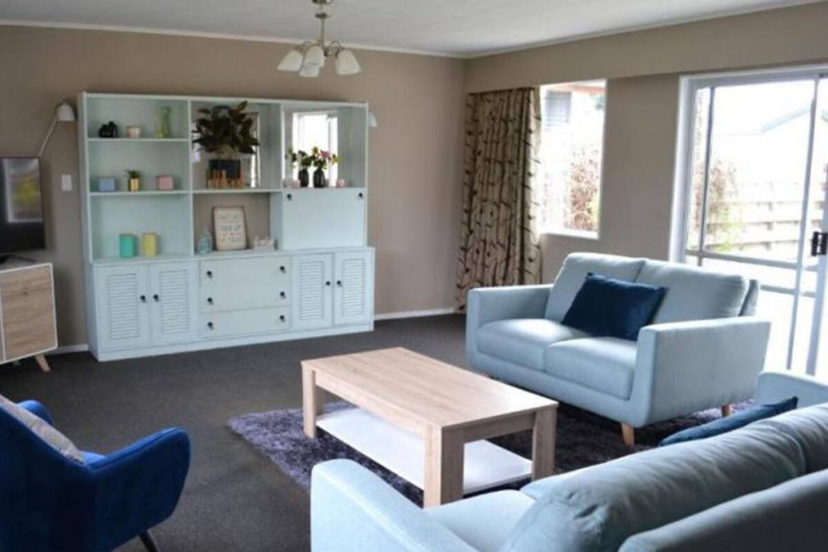 A living room with a television, a white cabinet with shelves, a blue armchair, a grey sofa, and a coffee table.
