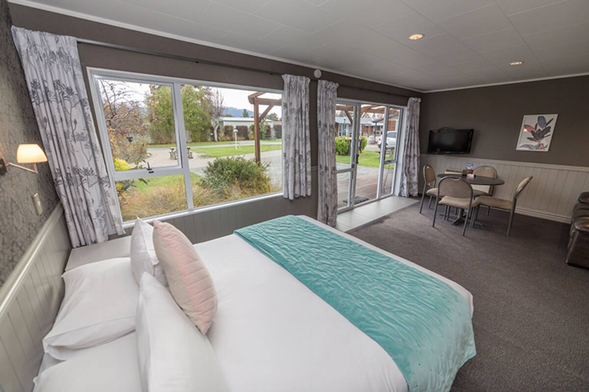 A hotel room with a large bed, a desk with chairs, a television, and a view of the outdoors.