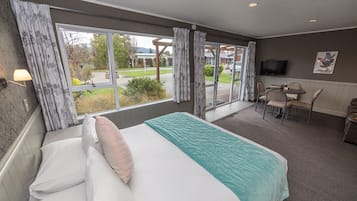 A hotel room with a large bed, a desk with chairs, a television, and a view of the outdoors.