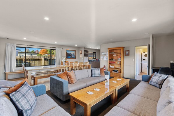 A modern living room with a sofa set, wooden coffee table, and a dining area with chairs and a table.