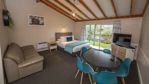 A bedroom with a bed, a desk, a TV, a sofa, and a window with curtains. - Tasman Holiday Parks - Te Anau (Te Anau)