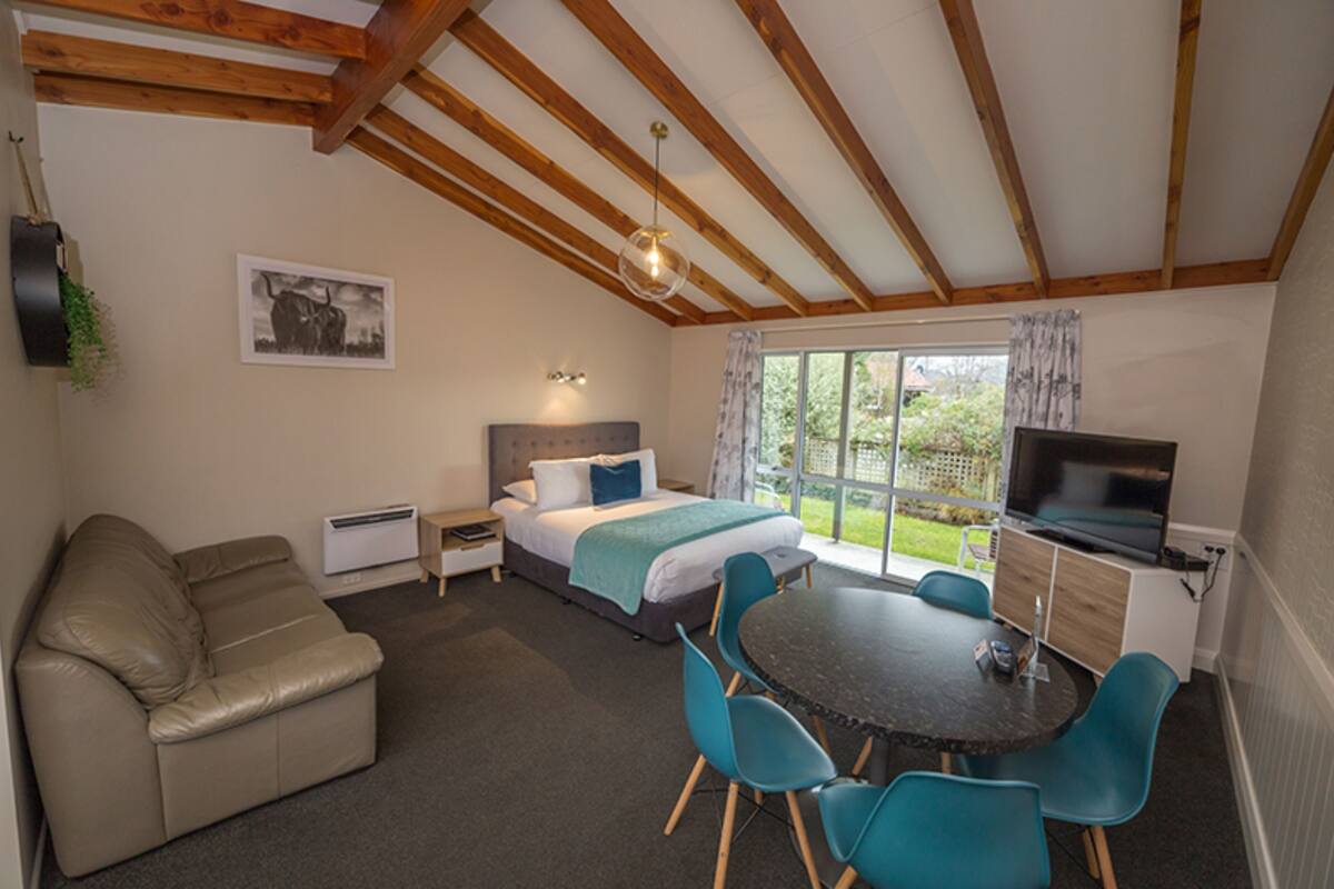 A bedroom with a bed, a desk, a TV, a sofa, and a window with curtains.
