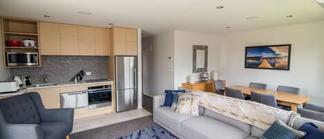 Et moderne køkken med indbyggede hårde hvidevarer, et spiseområde med et træbord og stole, samt en stue med sofa og et tæppe.