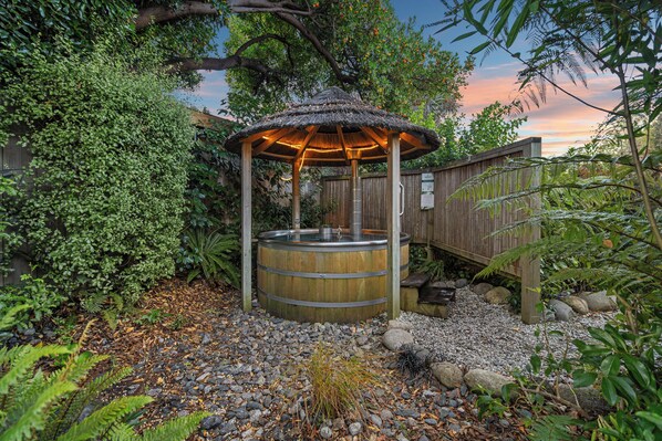A wooden gazebo with a thatched roof, surrounded by a garden with various plants and a wooden fence. - Tasman Holiday Parks - Te Anau (Te Anau)
