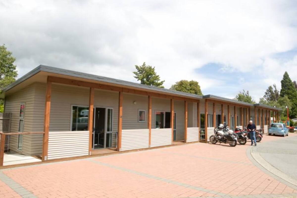 A motel with a row of rooms, a covered parking area, and a few motorcycles parked outside.