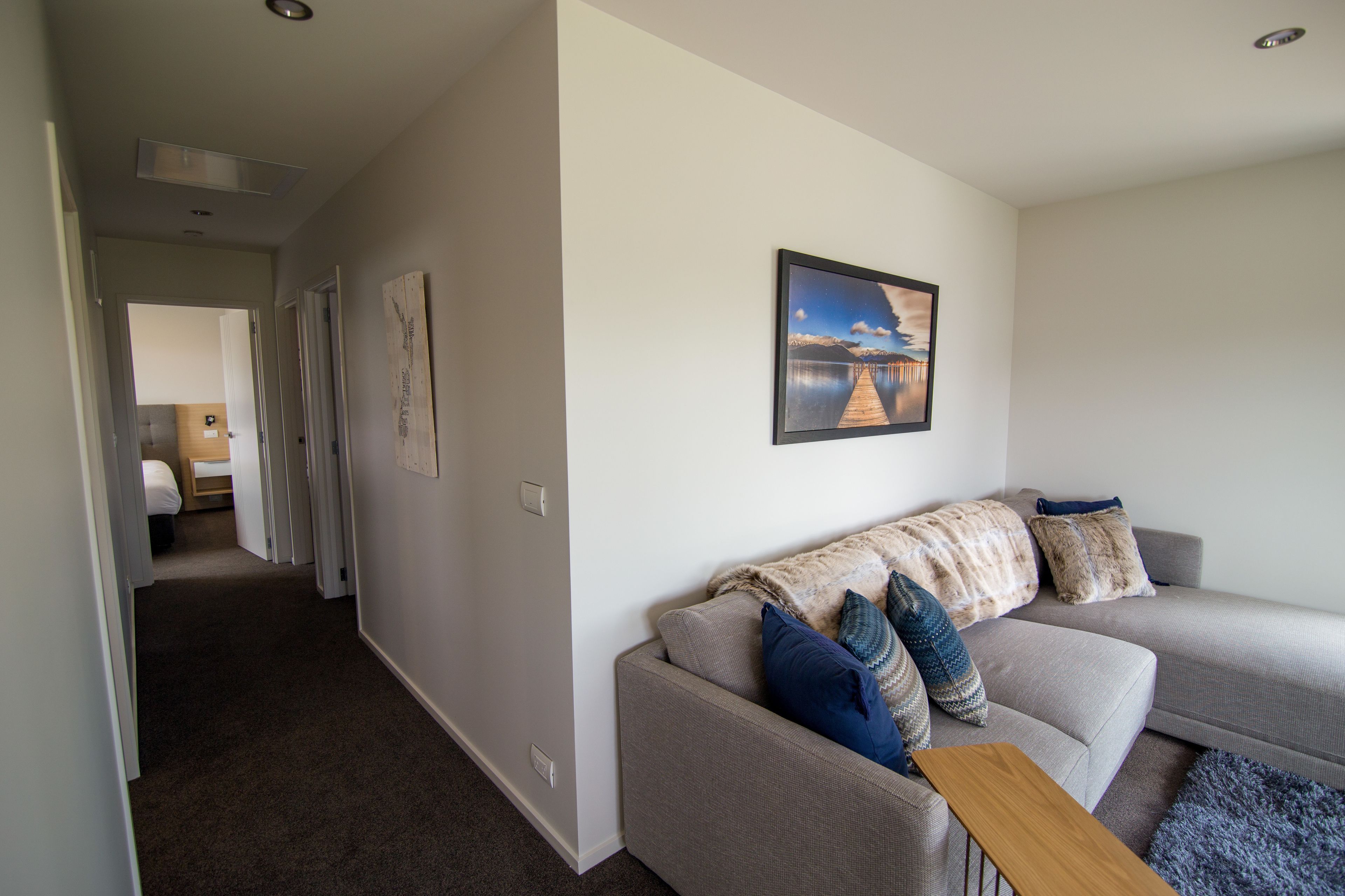 A modern living room with a grey sofa, a wooden coffee table, and a painting of a lake.