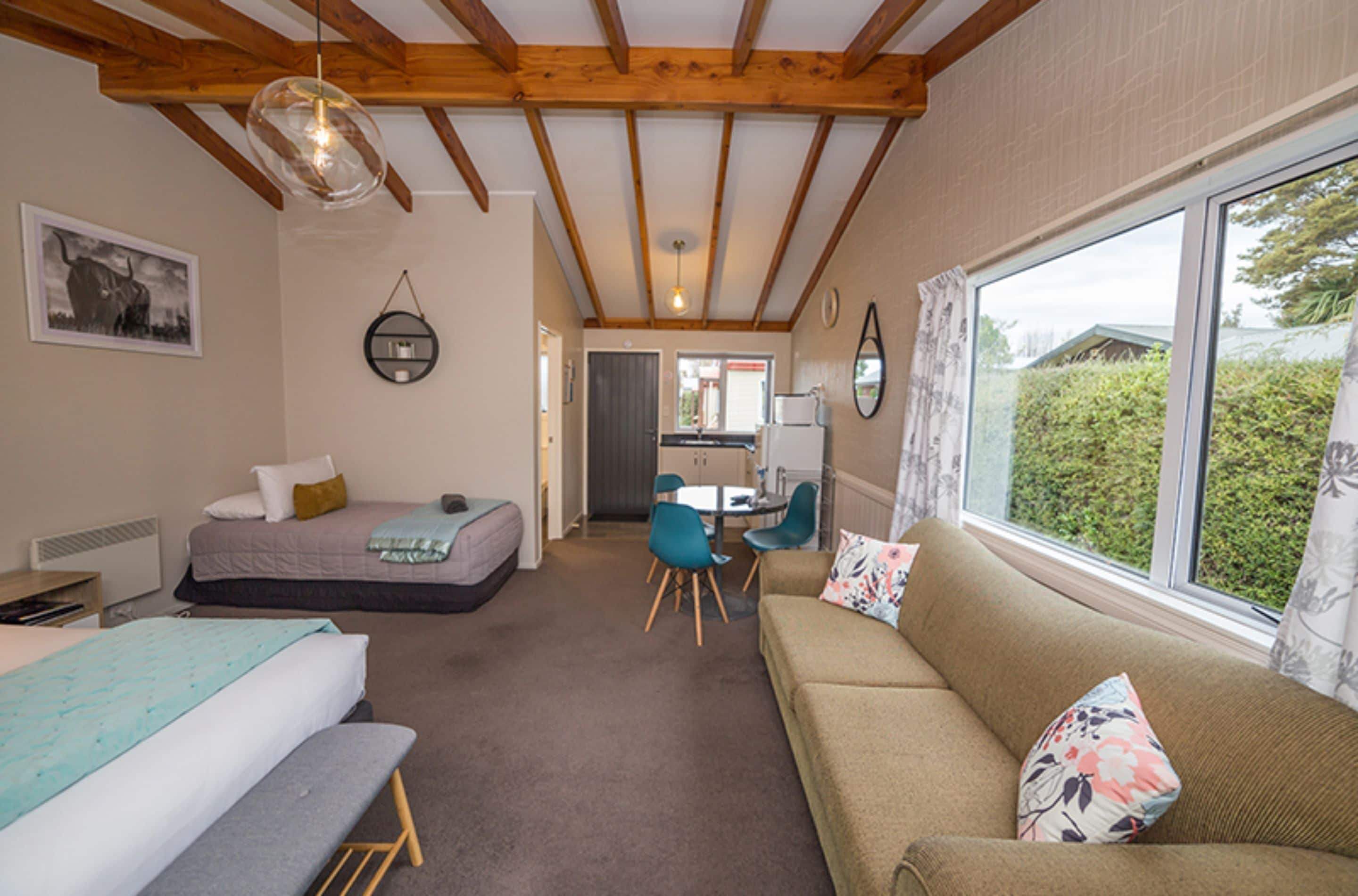 A cozy room with a bed, a sofa, a dining table with chairs, and a window with curtains.