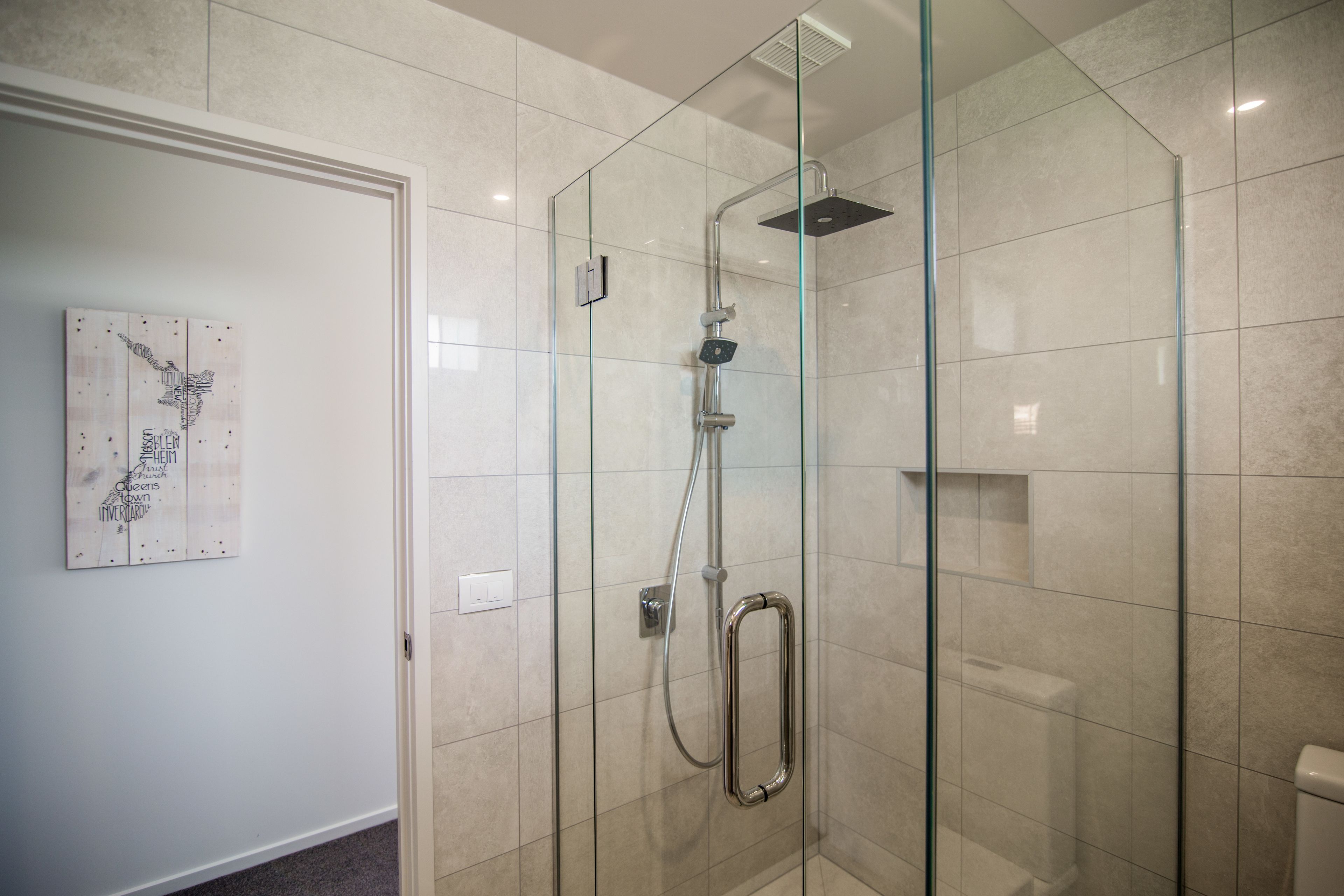 A glass-enclosed shower with a handheld showerhead and a square showerhead mounted on the wall.