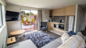 A modern kitchen with a built-in oven and microwave, a grey sofa, a small round table, and a TV mounted on the wall. - Tasman Holiday Parks - Te Anau (Te Anau)