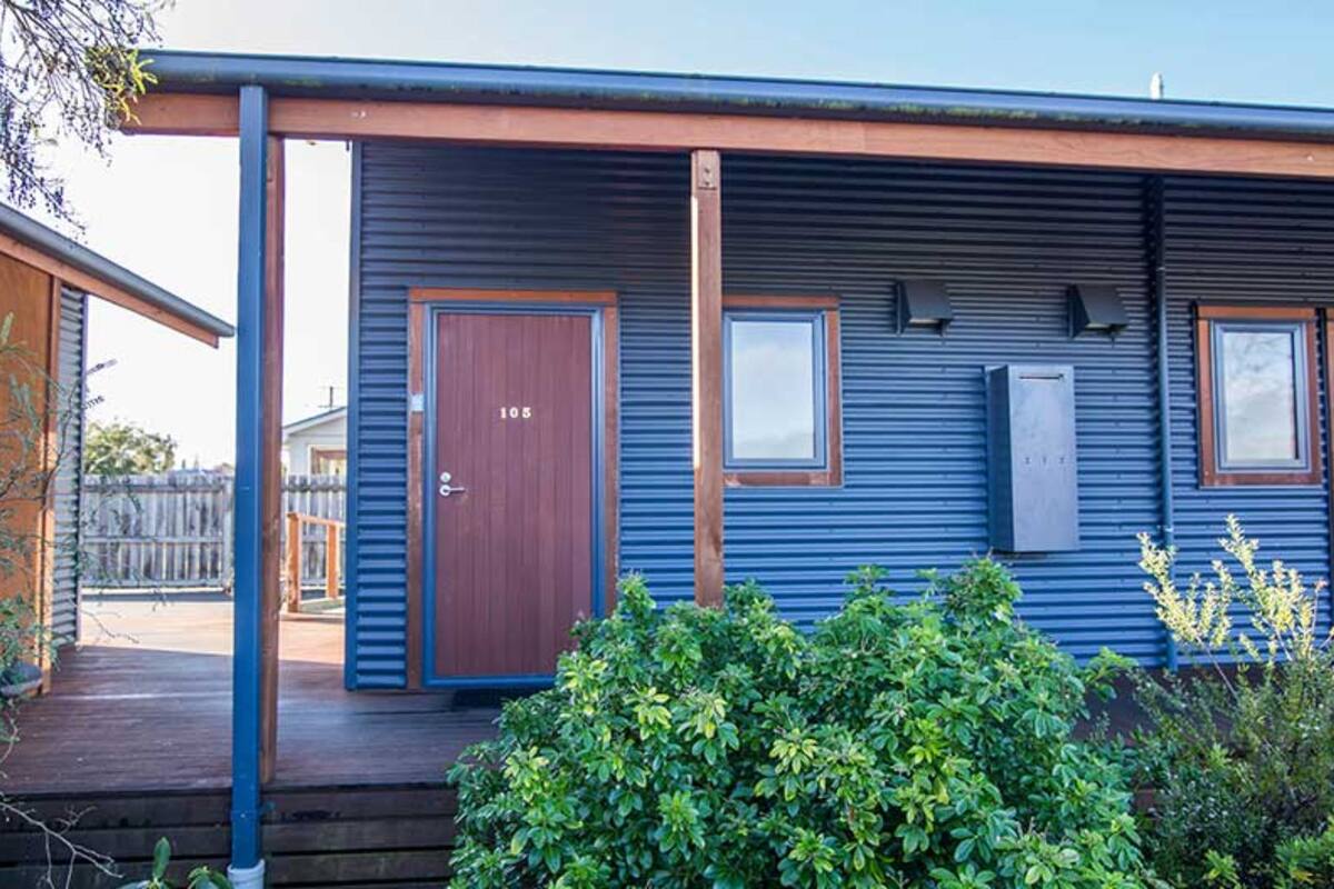 A blue building with a wooden door, two windows, and a small porch.