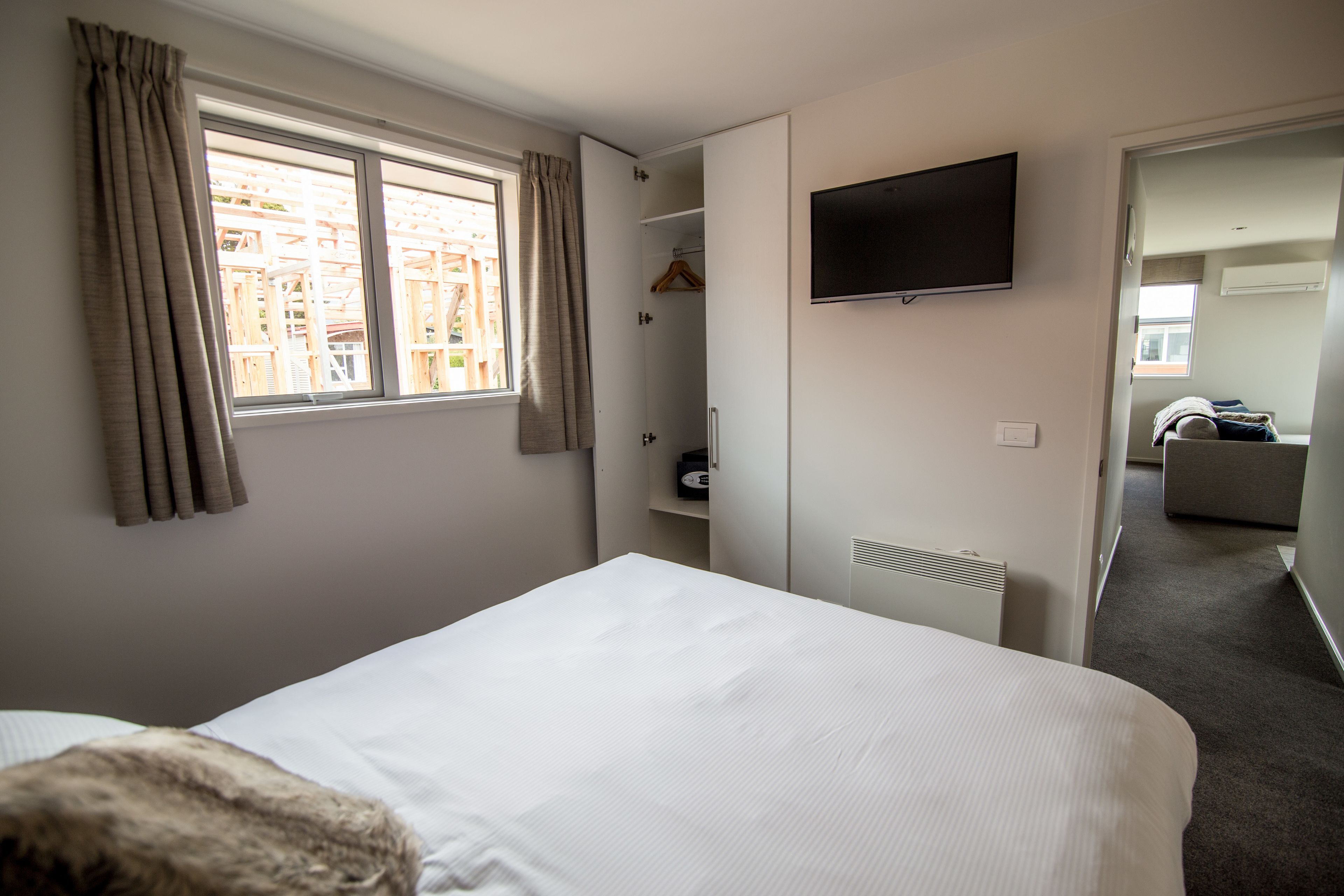 Una habitación de hotel con una cama, un televisor en la pared, una ventana con cortinas y un armario con perchero.