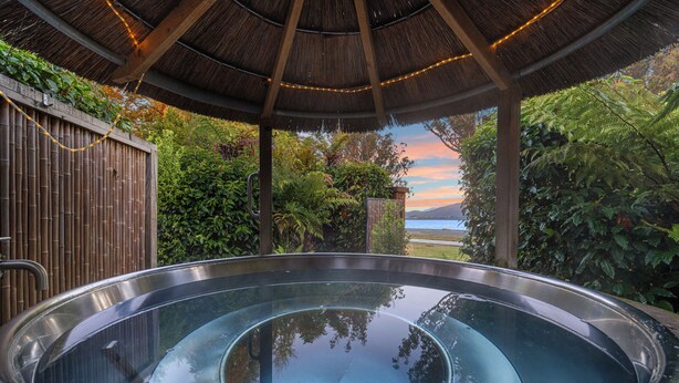 A hot tub under a thatched roof with bamboo fencing and lush greenery. - Tasman Holiday Parks - Te Anau (Te Anau)